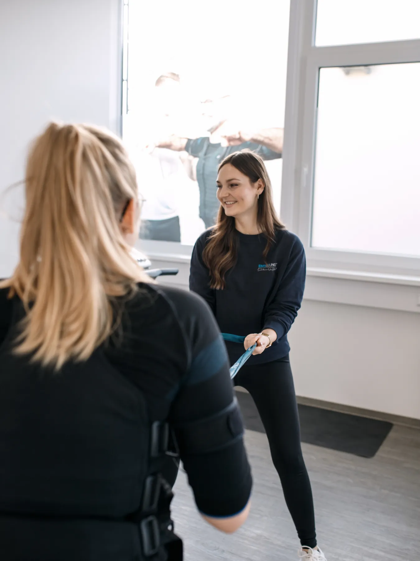Trainerin im Gespräch mit einer Kundin im EMS-Anzug, Reportage aus dem Studioalltag der EMS Lounge