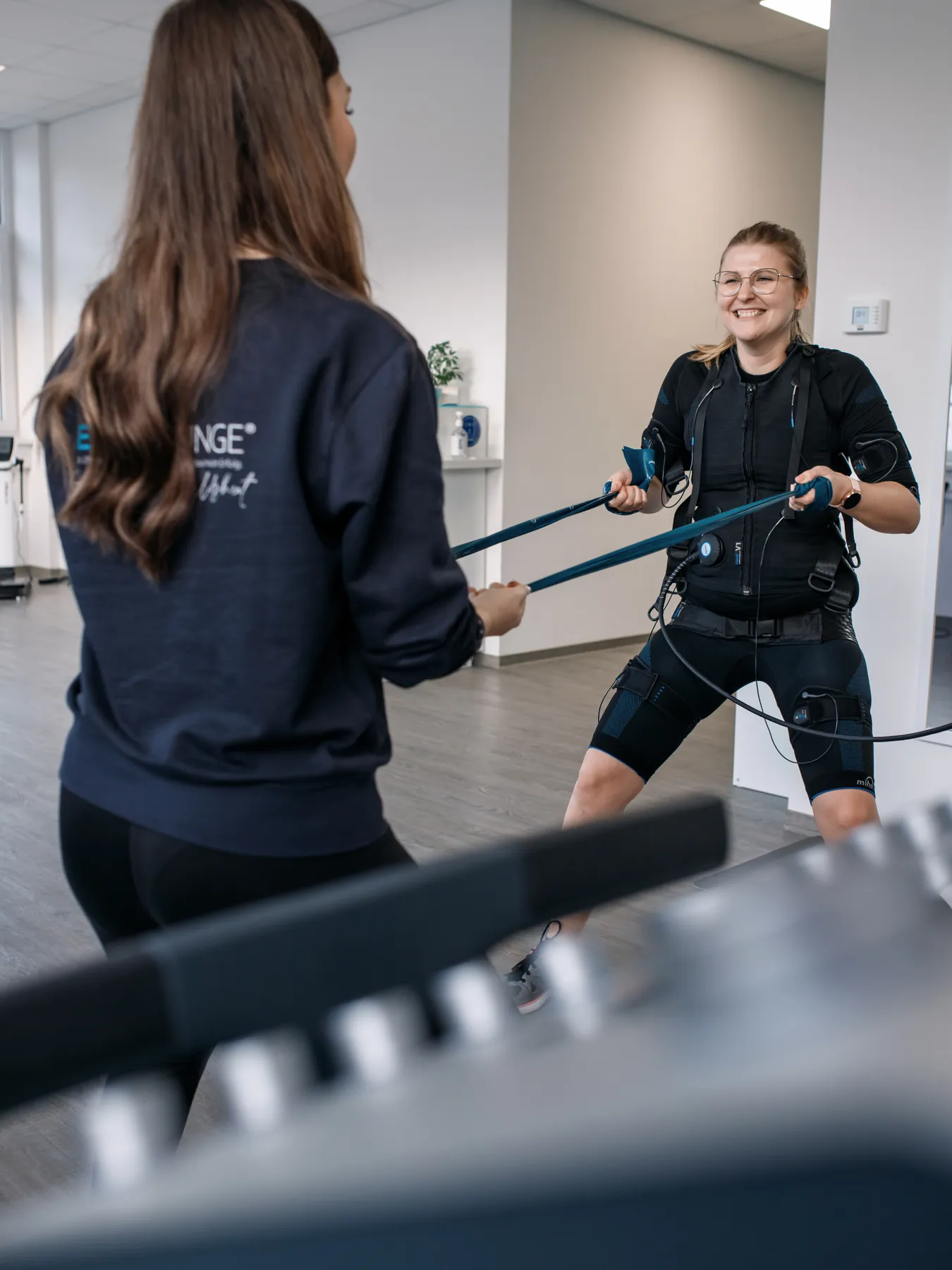 Trainerin der EMS Lounge leitet eine Kundin beim Training mit Zugbändern an, Businessfotografie von aLx-design