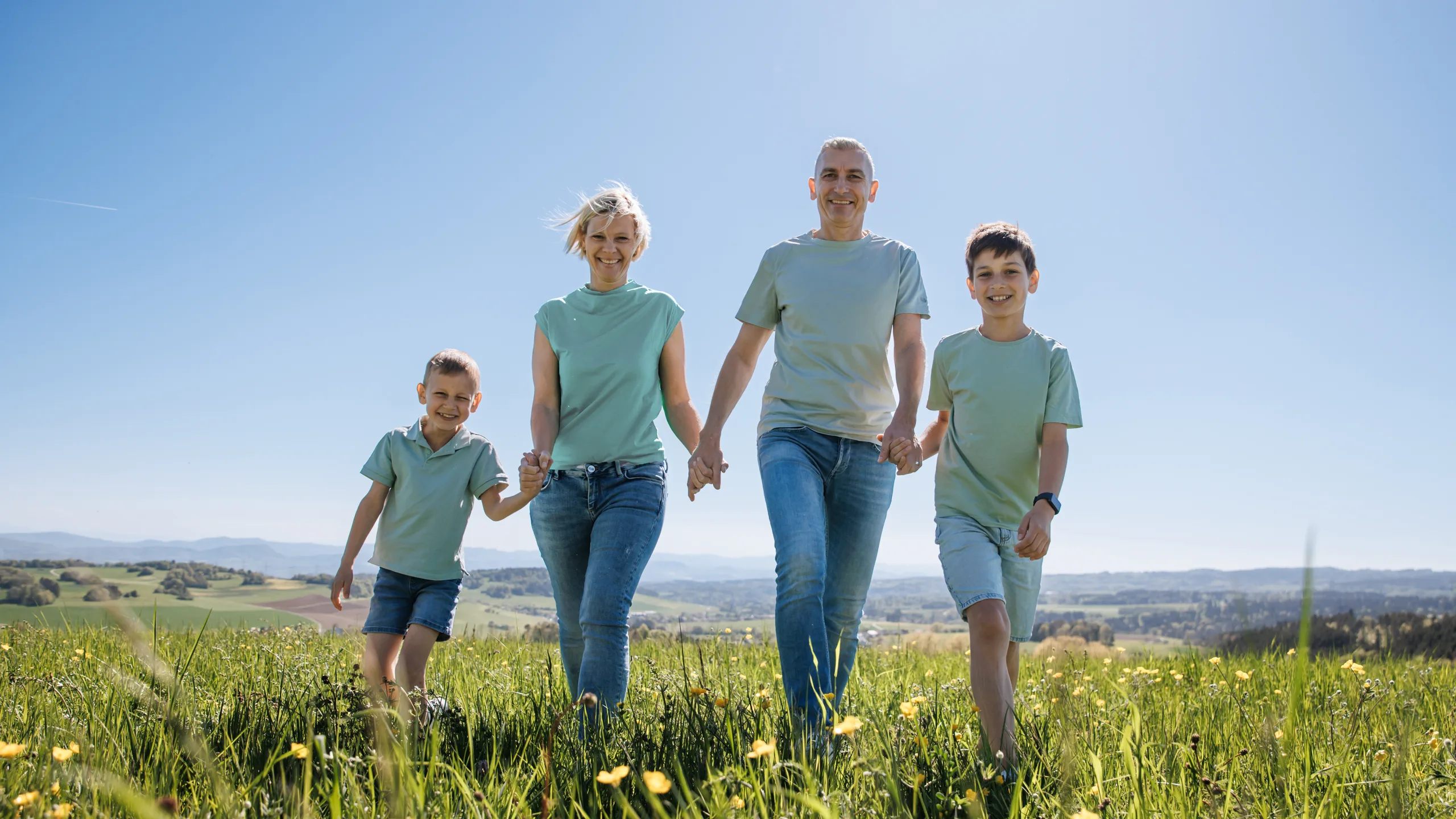 Familie geht Hand in Hand über eine Frühlingswiese über dem Hochrhein, Familienfotografie von aLx-design