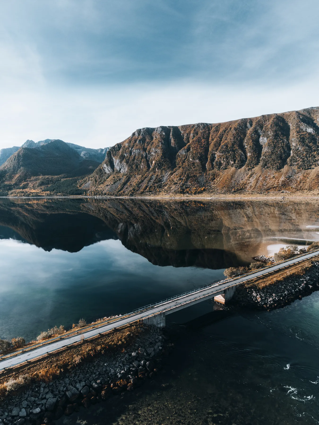 Drohnenaufnahme des Grunnførfjords auf den Lofoten mit Brücke und Bergen, die sich im Wasser spiegeln
