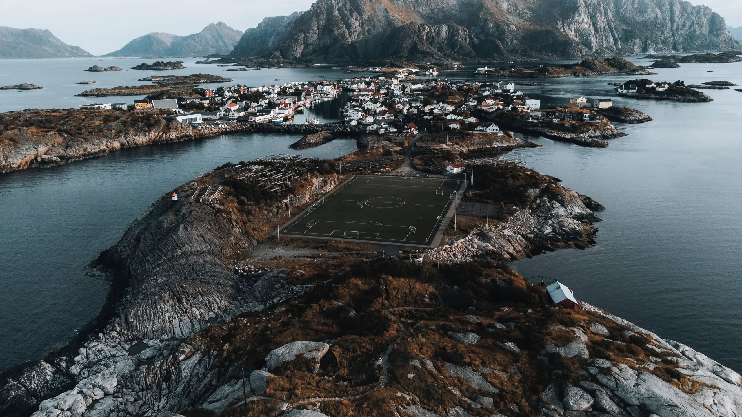 Drohnenaufnahme von Henningsvær auf den Lofoten mit dem Fussballplatz auf der Felsinsel und Bergkulisse, Spezialfotografie von aLx-design